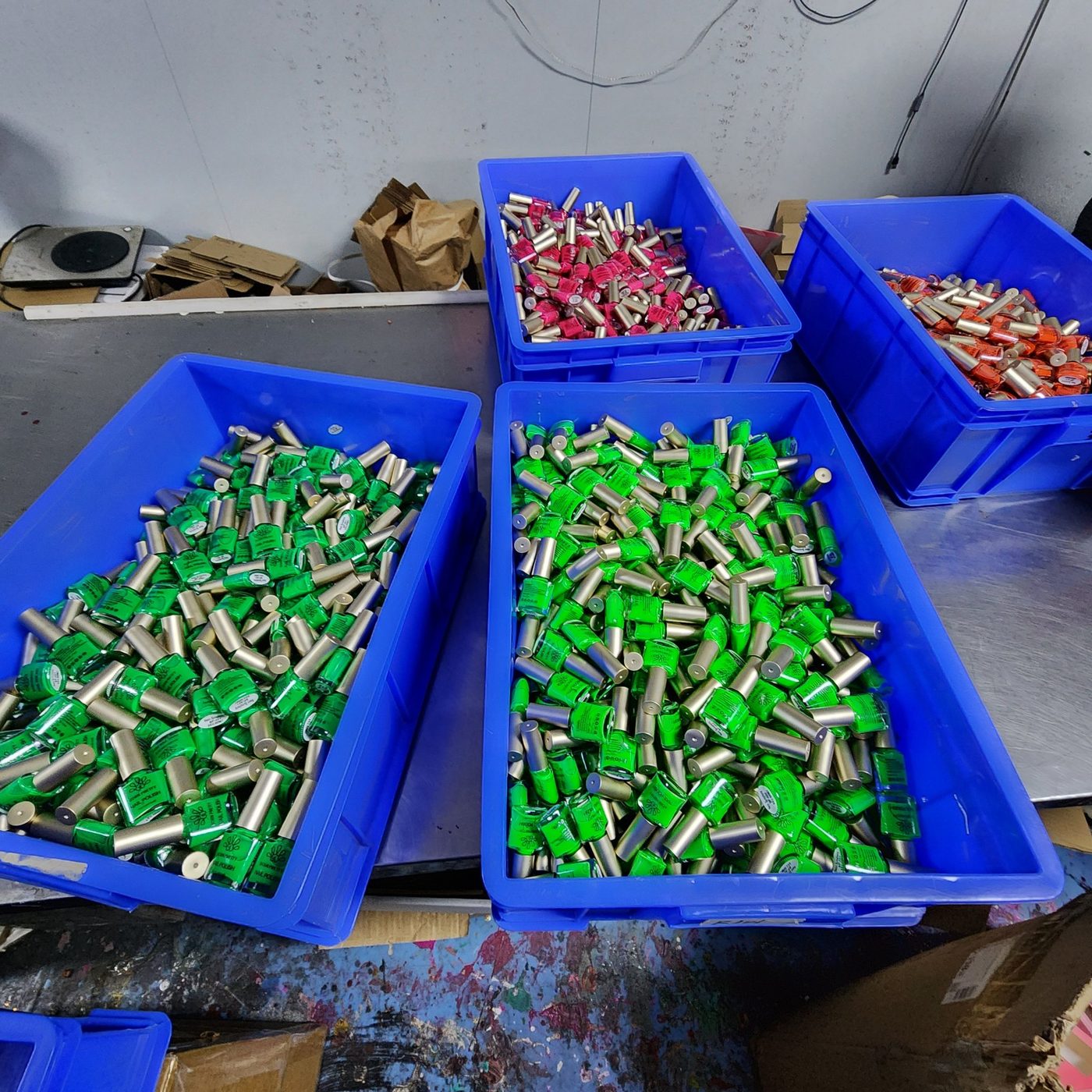 Bins of glow in the dark nail polish bottles in neon green, pink and coral on the factory floor